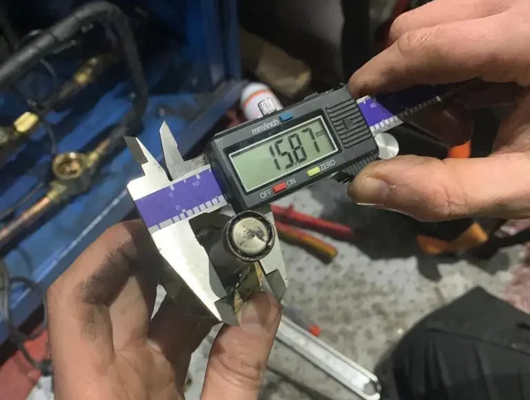 A person measuring a component using digital calipers